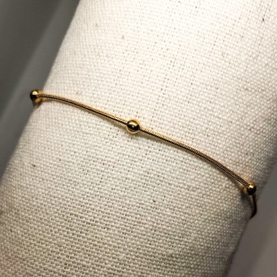 Pulseira dourada fina com três esferas em fundo branco