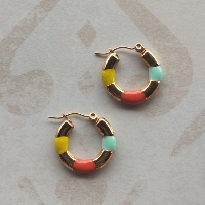 Brincos de argola dourados com segmentos coloridos sobre fundo claro com padrão