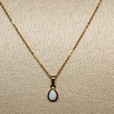 Colar dourado com pendente em gota branca sobre fundo bege