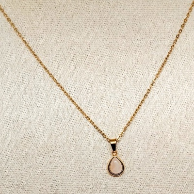 Colar dourado com pendente em forma de lágrima com pedra rosa sobre fundo bege
