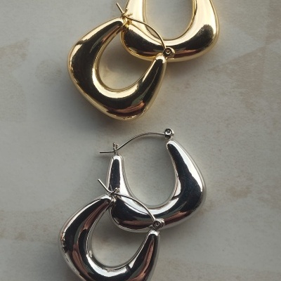 Dois pares de brincos ovais irregulares, um dourado e outro prateado, sobre fundo claro