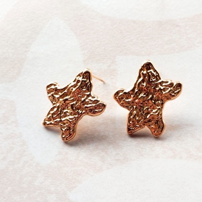 Brincos estrela dourados texturizados sobre superfície clara