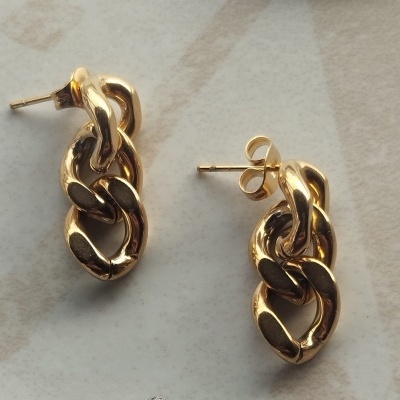 Brincos dourados de elos entrelaçados sobre superfície clara