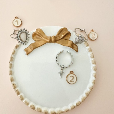 Três anéis prateados em prato branco com laço dourado e etiquetas numeradas