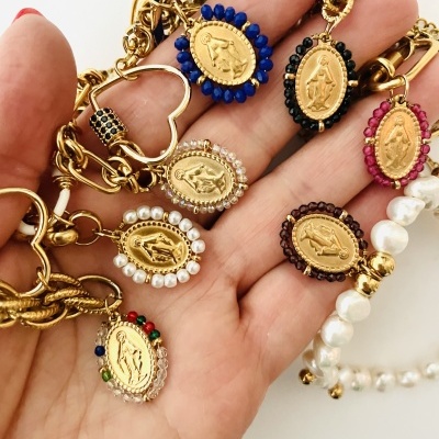Pulseiras douradas com medalhões religiosos e contas coloridas na mão.