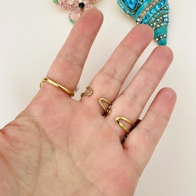 Mão com anéis dourados e broches decorativos em fundo branco