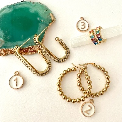 Três pares de brincos dourados com pendentes numerados e uma agata verde ao lado