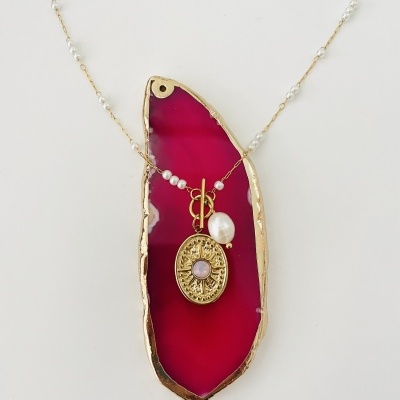 Colar dourado com pérolas e pendente oval com pedra rosa sobre pedra decorativa vermelha