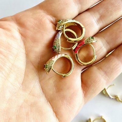 Conjunto de brincos dourados com detalhes verdes na mão sobre fundo branco