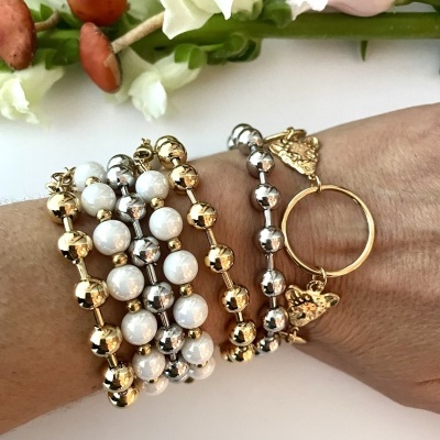 Bracelete com contas douradas, prateadas e brancas com pingentes de borboleta no pulso