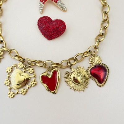 Colar dourado com pendentes em forma de coração e broches vermelhos em fundo branco