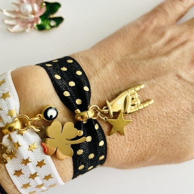 Pulseiras de tecido com pendentes dourados na mão e broche de flor ao fundo