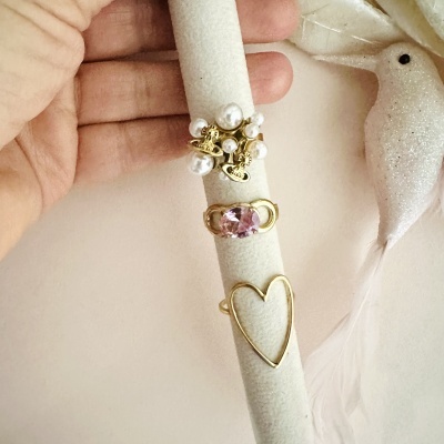 Três anéis em suporte de veludo bege, com pérolas, pedra rosa e forma de coração