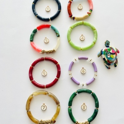 Oito pulseiras coloridas numeradas de 1 a 8 sobre fundo branco, junto a um chaveiro de tartaruga colorida