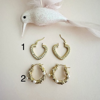 Dois pares de brincos dourados numerados a 1 e 2, junto a pássaro decorativo branco com glitter.