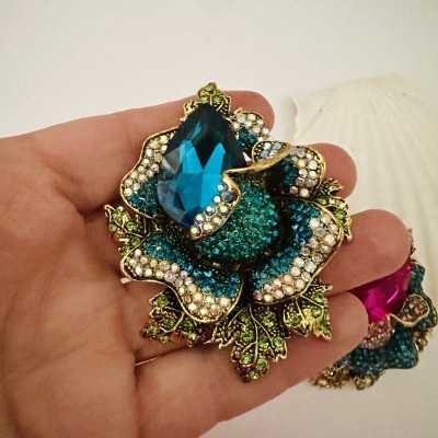 Broche flor azul com pedras brilhantes e grande pedra azul no centro numa mão.