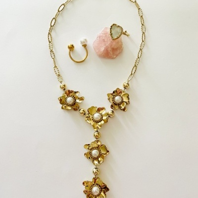 Colar dourado com flores e pérolas, anel dourado e pedra rosa sobre fundo branco