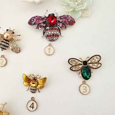 Quatro pins de abelhas com pedras coloridas e etiquetas numeradas