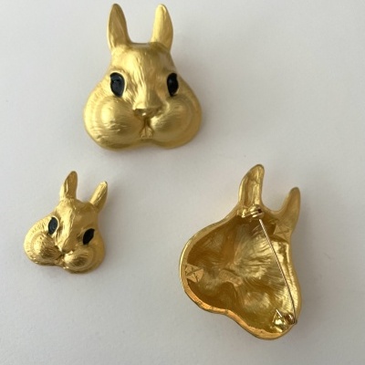 Broches dourados em forma de cabeça de coelho com olhos pretos, sobre fundo branco