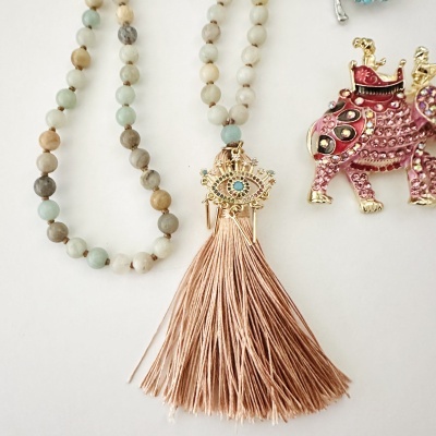 Colar de contas pastel com pingente de olho e franja cor de rosa, ao lado de um broche rosa de camelo brilhante