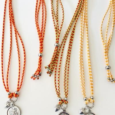 Três colares com cordão trançado laranja e amarelo e medalhões metálicos prateados.