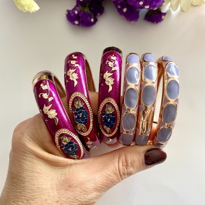 Pulseiras coloridas em vermelho vinho e lilás com detalhes dourados, seguradas por mão feminina.