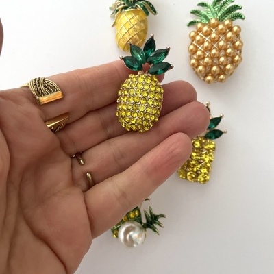 Broches de ananás dourados e verdes exibidos sobre fundo branco