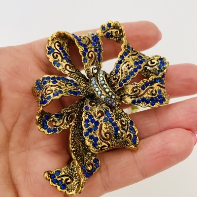 Broche dourado em formato de laço com pedras azuis e claras