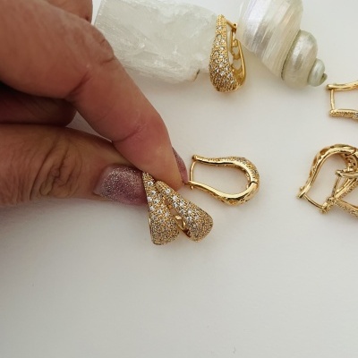 Brincos dourados com pedras brilhantes em superfície branca com pedras e conchas