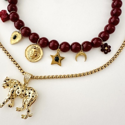 Dois colares, um com contas vermelhas e vários pendentes dourados, outro com pingente de leopardo dourado em fundo branco.