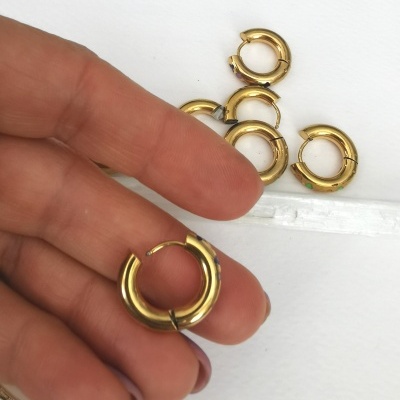 Brincos argola pequenos dourados em fundo branco com mão a segurar um deles