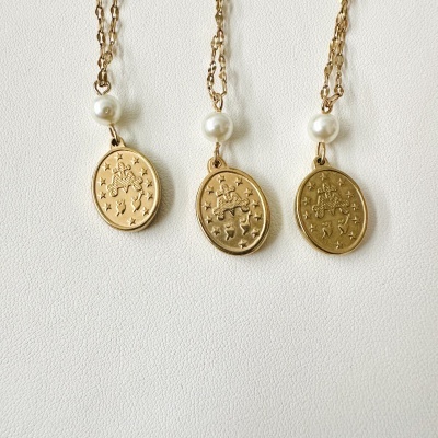 Três colares dourados com pendentes ovais e pérolas em fundo branco