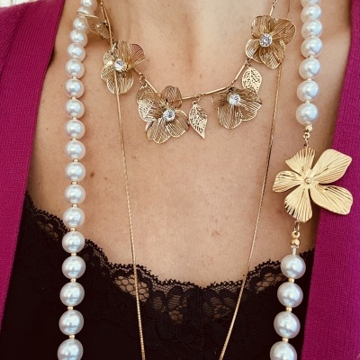 Colares dourados com flores e pérolas em pescoço feminino com roupa rosa e preta