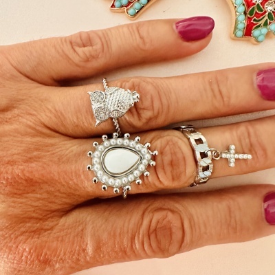Três anéis prateados em dedos com unhas roxas, detalhe em coruja, gota e cruz com pérolas