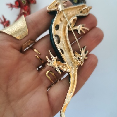 Broche lagarto dourado azul preto na mão com fundo branco e broches desfocados