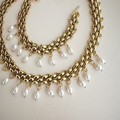 Conjunto de colar e pulseira dourados com pérolas brancas penduradas.