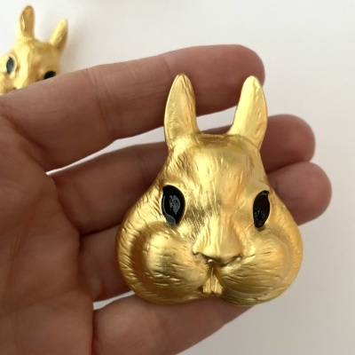 Figurinha de cabeça de coelho dourada com olhos pretos segurada por mão