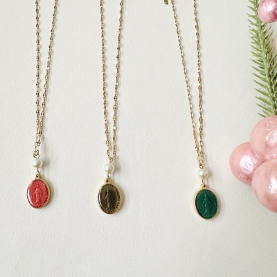 Três colares dourados com pendentes ovais coloridos e pérolas, sobre fundo branco com decoração verde e rosa