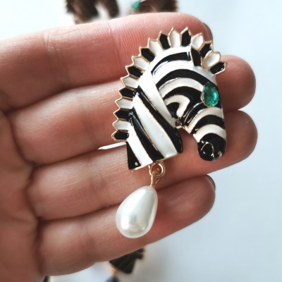 Brinco em forma de cabeça de zebra com pendente perolado numa mão