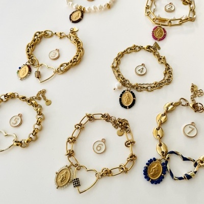 Sete pulseiras douradas com pendentes ovais coloridos e uma pulseira branca, todas numeradas de 1 a 7