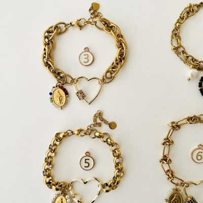 Pulseiras douradas de elos grossos com pendentes religiosos e corações, numeradas com etiquetas 3, 5 e 6