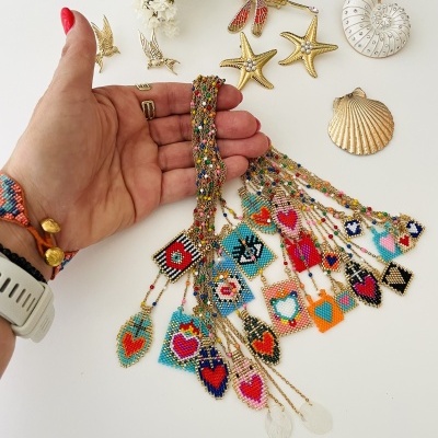 Colar colorido artesanal com pingentes de contas em forma de corações e acessórios dourados marinhos em fundo branco.