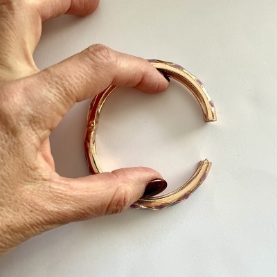 Pulseira rígida dourada com esmalte roxo segurada por mão feminina