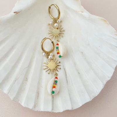 Brincos dourados com sol, pérolas e conchas coloridas sobre uma concha branca grande