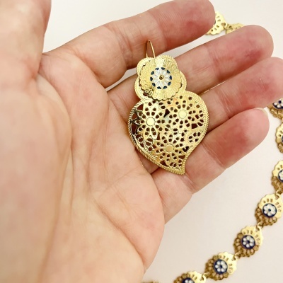 Brinco dourado pendente floral com aplique azul e branco na mão