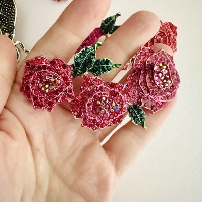 Joia floral vermelha com pedras brilhantes e folhas verdes numa mão