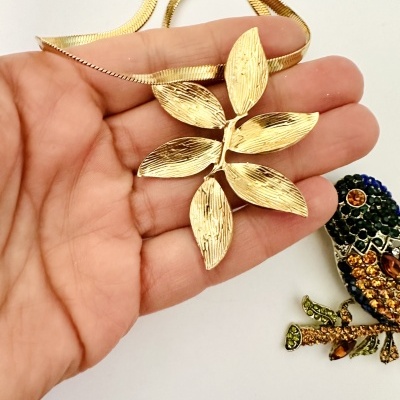 Colar dourado com pendente em forma de folha segurado por uma mão