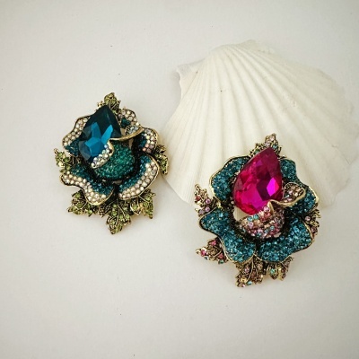 Dois broches com pedras azuis e rosa em fundo branco com concha