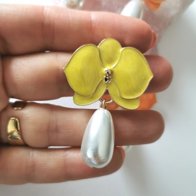 Brinco flor amarela com pérola pendente e mão segurando