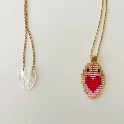 Dois colares dourados com pendentes distintos, um transparente oval e outro em padrão pixelado cor de rosa com coração vermelho.